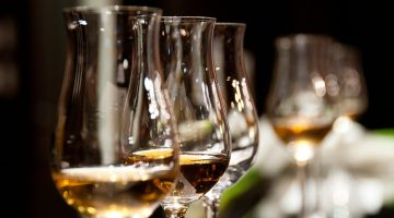 Regal Cask's three whisky investment tiers: Blue-Chip Core with gold cask and stability chart; Growth Portfolios showing green upward arrow; Club-Exclusive featuring premium tasting glass—all against elegant dark oak whisky warehouse texture with golden lighting.