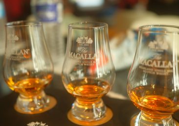 Single oak cask in maturation warehouse Stenciled whisky cask with distillery markings Aged Scotch whisky cask ready for investmentshowing green upward arrow; Club-Exclusive featuring premium tasting glass—all against elegant dark oak whisky warehouse texture with golden lighting.